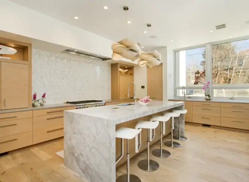 bright, modern kitchen with large wood cabinets, unique light fixtures, and marble island with white stools ONE Residential Builders Denver