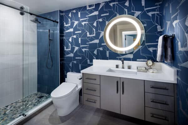bathroom in Highlands Ranch has modern flair with blue and silver wall, blue and gray tile, and circle mirror ONE Residential Builders Denver