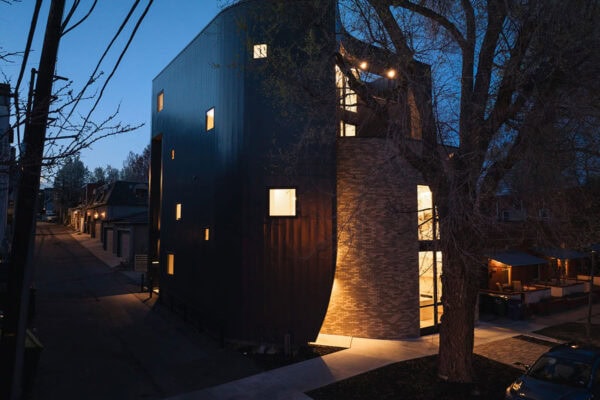 nighttime view of contemporary home with brick and metal siding outside, several small windows on one side, and large windows on the other side ONE Residential Builders Denver