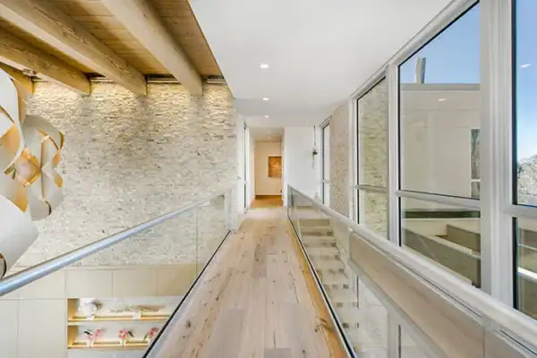 hallway of modern home with wood flooring, wood ceiling paneling and glass railings ONE Residential Builders Denver